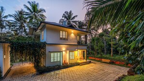 A two-story house with a paved driveway, a balcony, and a well-lit entrance. - Exuberance Stays (Sulthan Bathery)