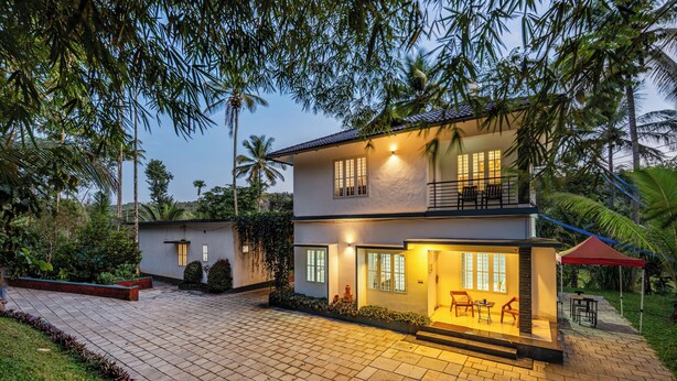 A two-story house with a balcony, a patio with outdoor furniture, and a well-maintained garden. - Exuberance Stays (Sulthan Bathery)