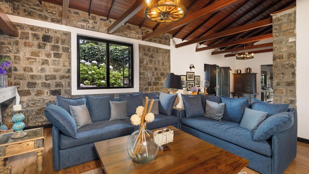 Un salon avec un canapé d’angle bleu, une table basse en bois et un mur en pierre.