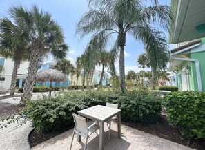 A patio area with a table and chairs, surrounded by palm trees and shrubs. - Margaritaville Luxe Cottage • 2 Master Suites • Disney ~5m • Walk to Fun & Eats (Kissimmee)