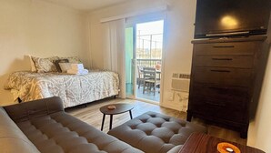 Et hotelværelse med sofa, et lille bord, en seng med mønstret sengetøj, et klædeskab og udsigt gennem en glasdør.