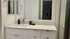 Et moderne badeværelse med en hvid kommode, et stort spejl og en lampe over spejlet.