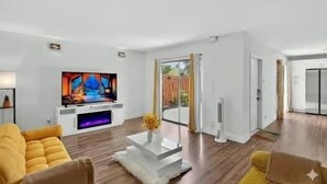En moderne stue med et fladskærms-tv, en sofa, et sofabord og en skydedør, der fører til et udendørs område.
