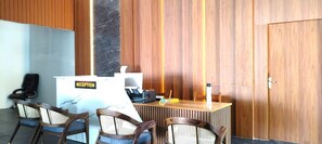 A reception desk with a sign, wooden panel walls, a door, and four chairs. - MOON LIGHT RESORT (Idappadi)
