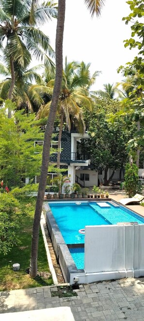 A swimming pool surrounded by palm trees and greenery, with a building in the background. - MOON LIGHT RESORT (Idappadi)