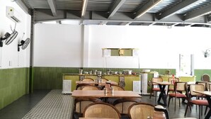 A restaurant with green and white walls, tables with wicker chairs, and a counter with kitchen equipment. - MOON LIGHT RESORT (Idappadi)
