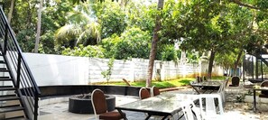 An outdoor dining area with tables and chairs, surrounded by a stone wall and greenery. - MOON LIGHT RESORT (Idappadi)