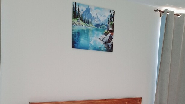 Quarto com cama de madeira, duas mesas de cabeceira com luminárias, um quadro na parede e um tapete redondo no chão.