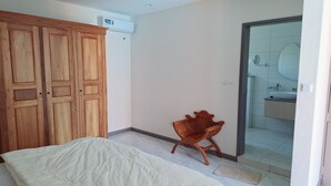 Quarto com cama, guarda-roupa de madeira e uma cadeira. Dá para ver um banheiro por uma porta aberta.