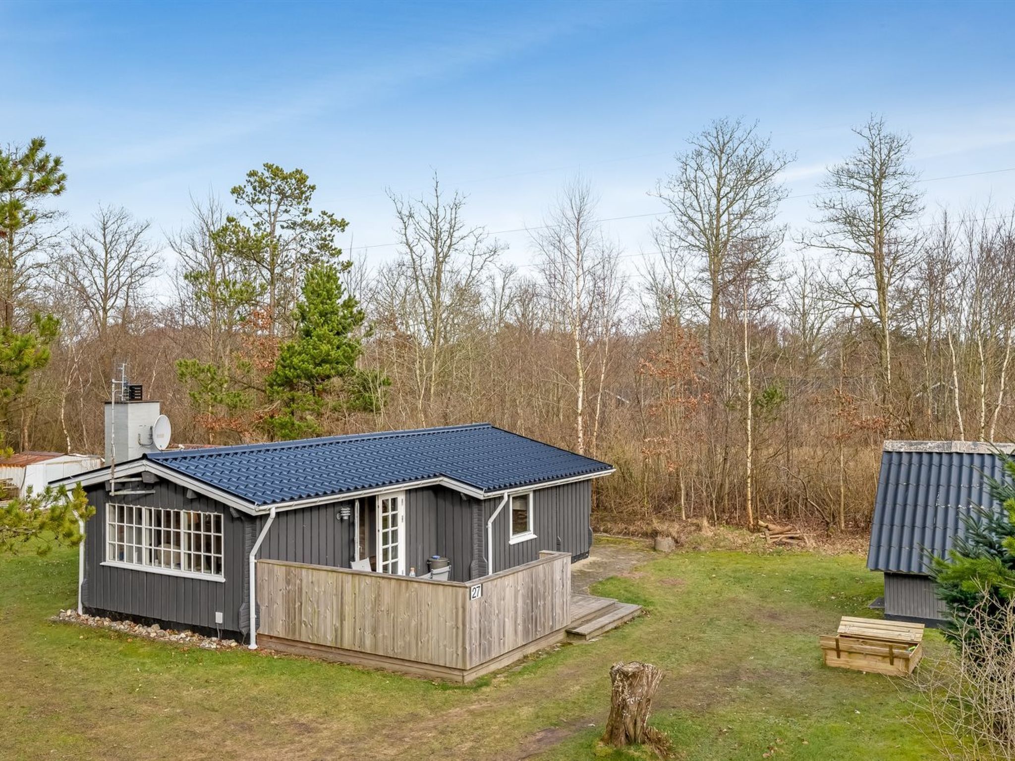A single-story house with a dark roof and gray siding, surrounded by a wooden deck and a fenced yard.