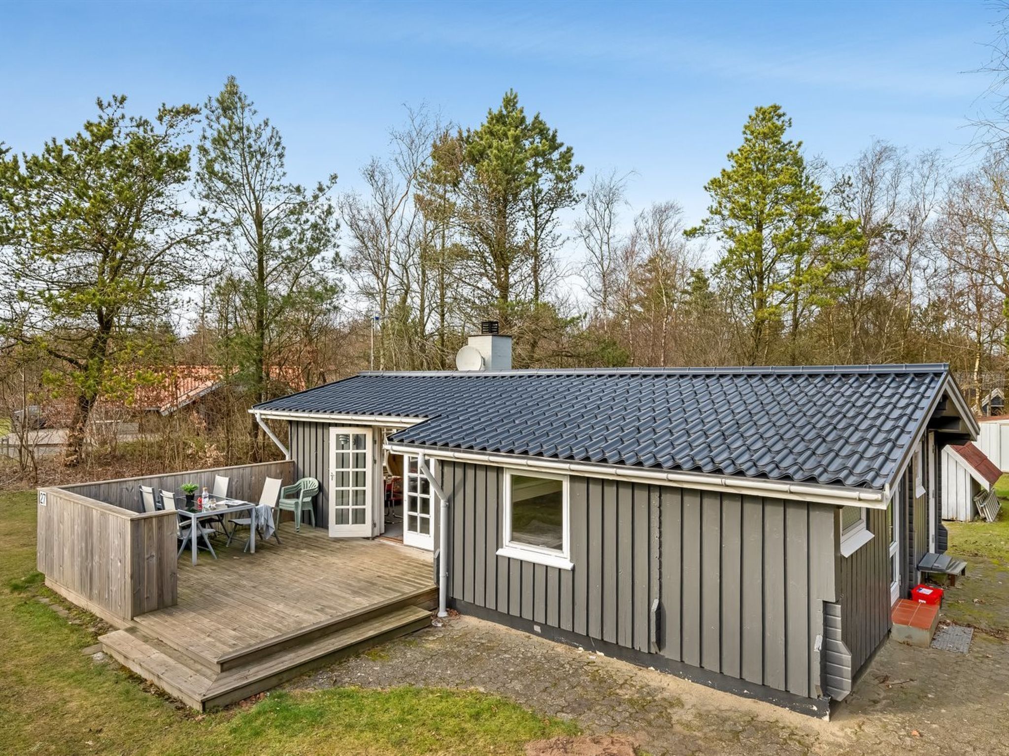 Il s’agit d’un petit bâtiment d’un seul étage, à l’extérieur de couleur gris foncé et doté d’un toit en tuiles. On y trouve une terrasse en bois avec des meubles d’extérieur et un petit espace patio.