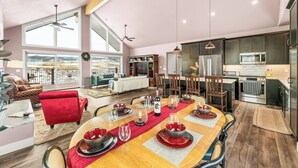 Een ruime woonkamer met een grote eettafel voor zes personen, een gezellige zithoek met een rode bank, en een keuken met moderne apparatuur.