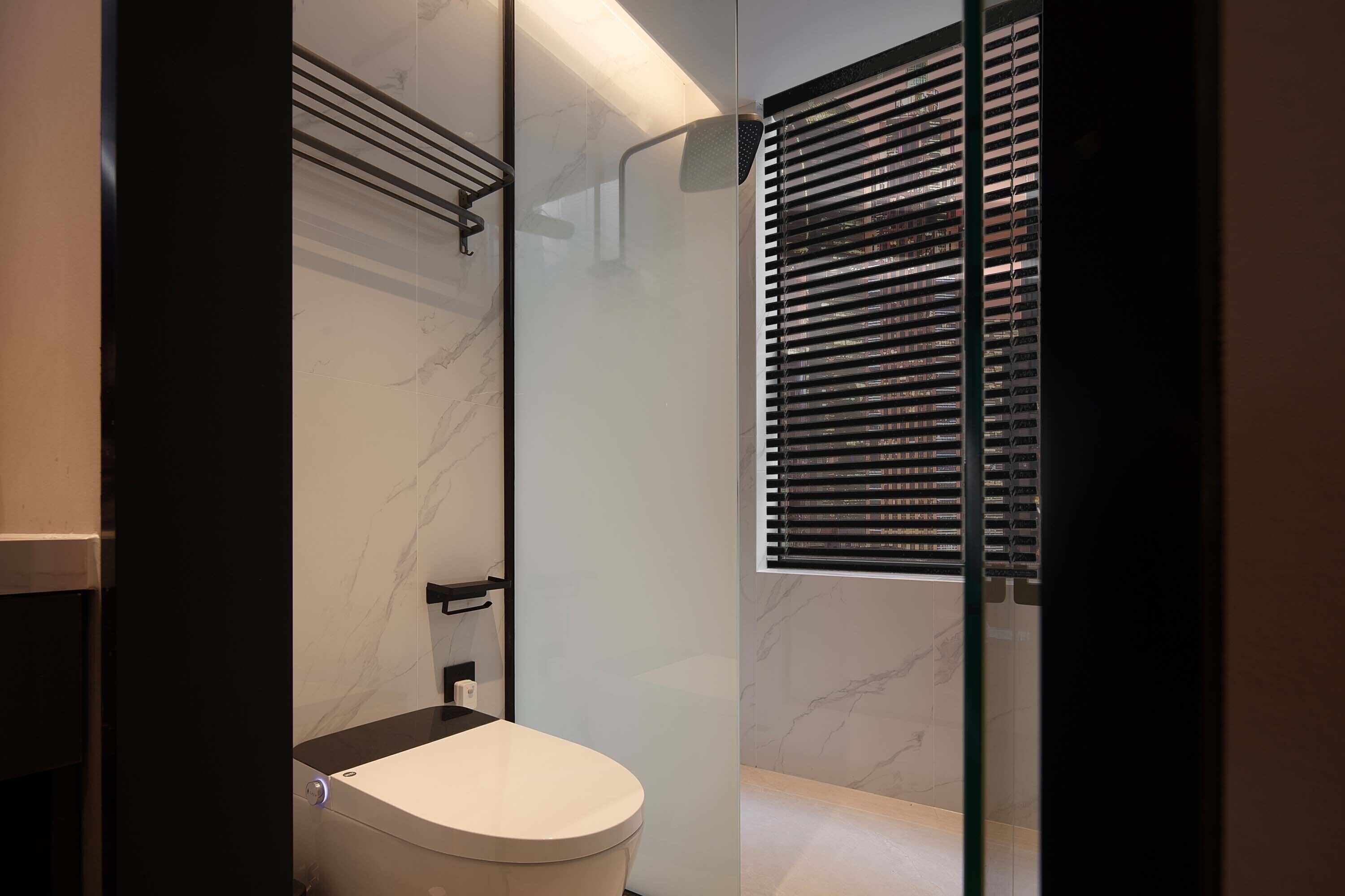 A modern bathroom with a toilet, a shower with a glass door, and a window with blinds.