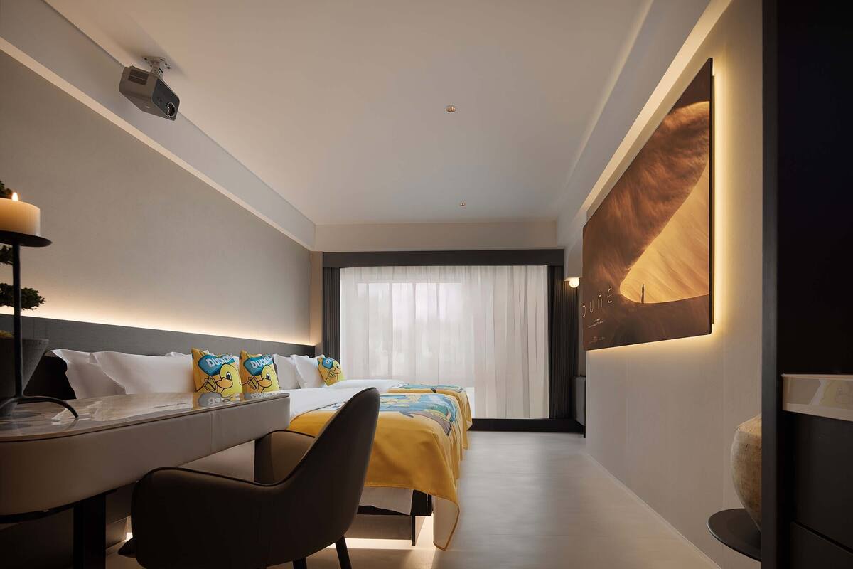 Een moderne hotelkamer met een bed, een bureau en een groot raam met transparante gordijnen.