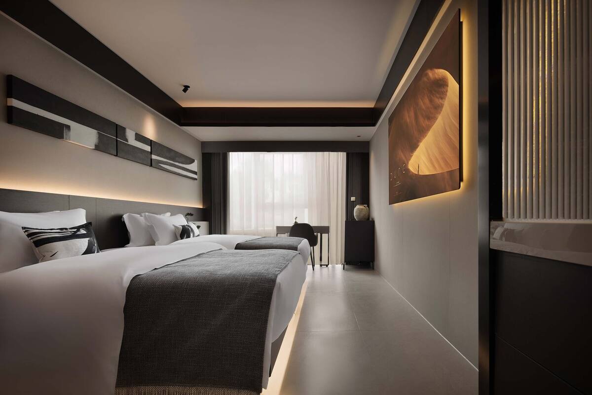 Een moderne hotelkamer met een groot bed, een bureau en een groot raam met dunne gordijnen.