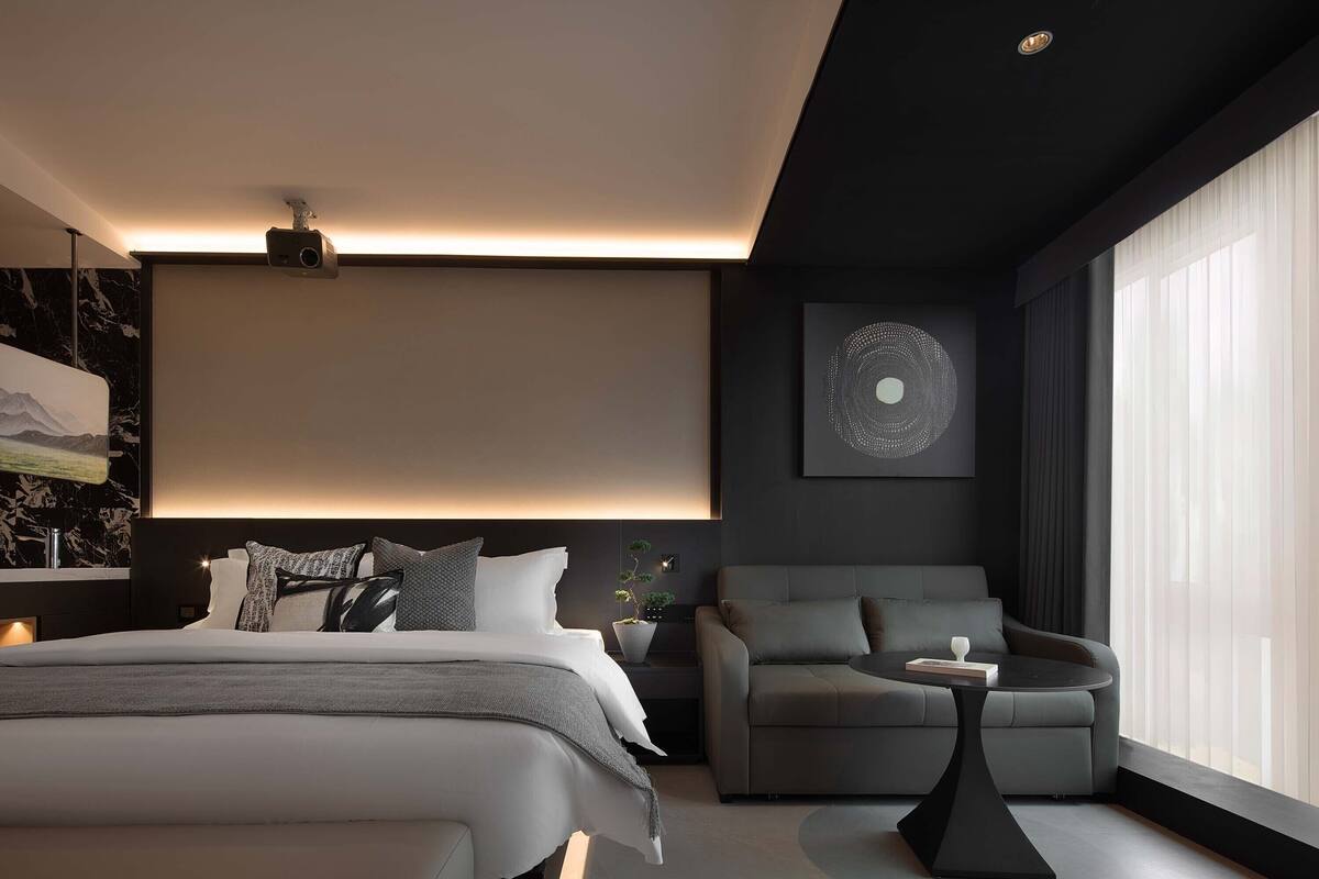 Een moderne slaapkamer met een groot bed, een sofa, een klein tafeltje en een projector aan het plafond.