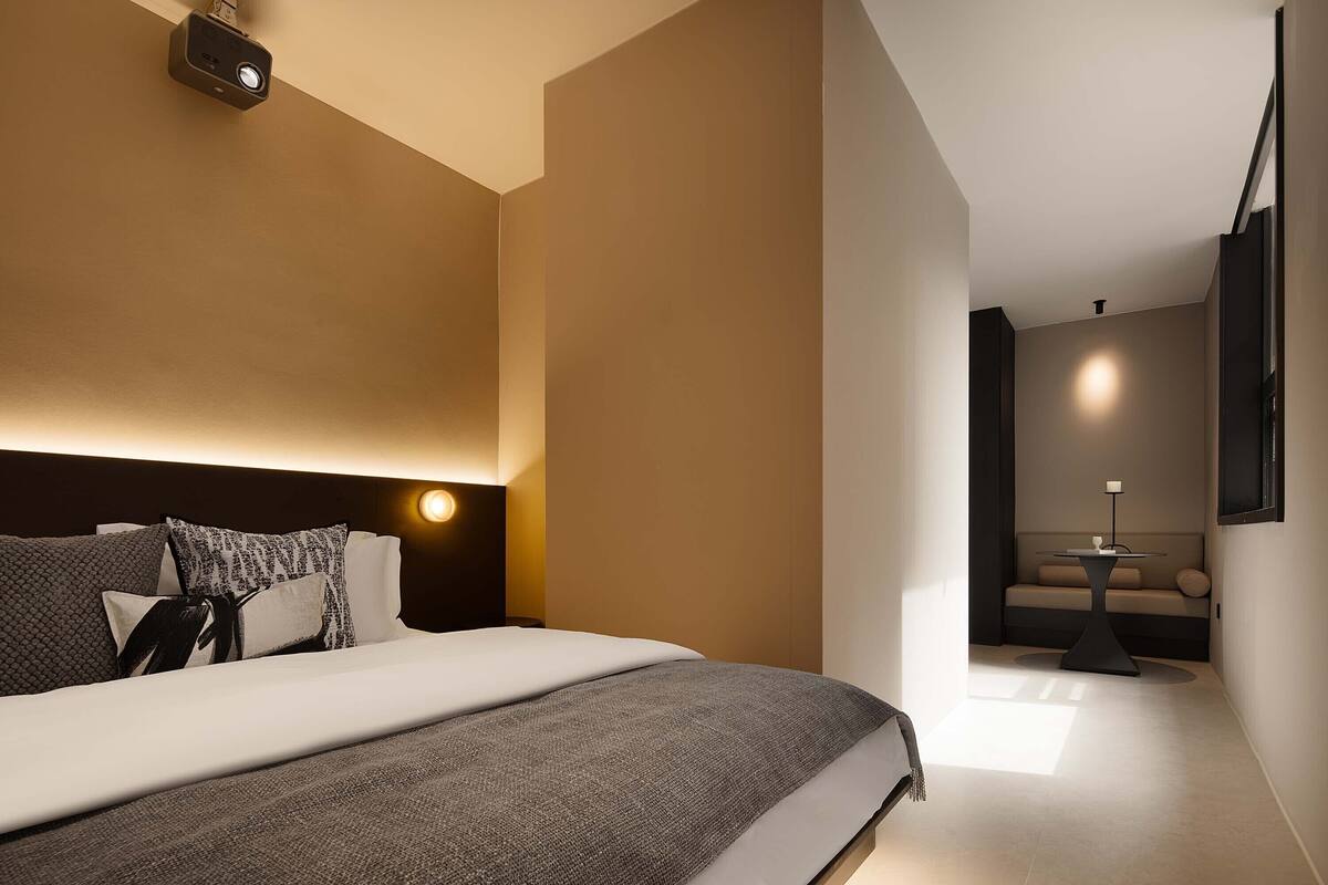 Een moderne hotelkamer met een groot bed, een nachtkastje, een wandlamp en een bank op de achtergrond.