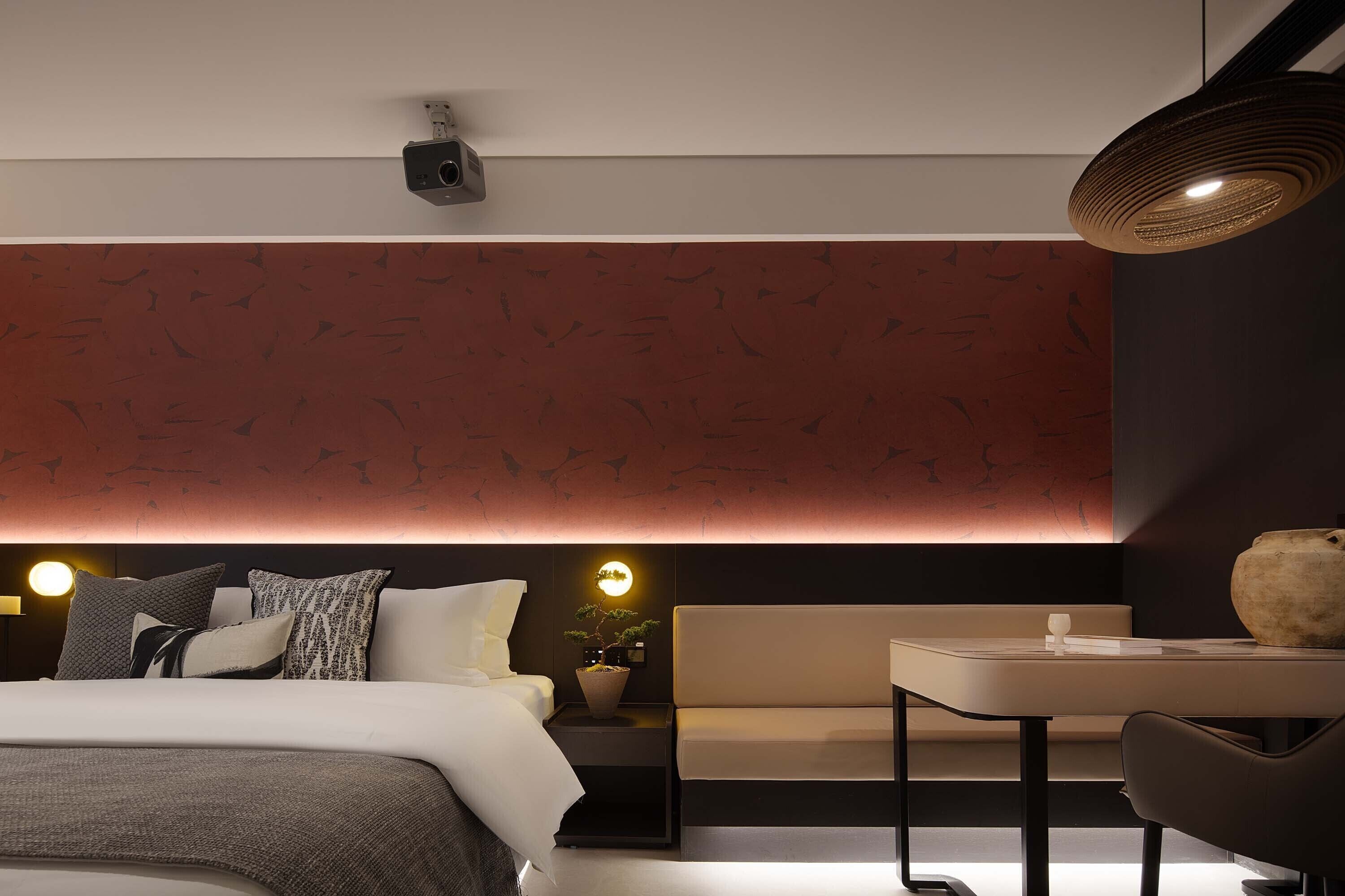 Una habitación de hotel moderna con cama, mesita de noche y un pequeño rincón de descanso.