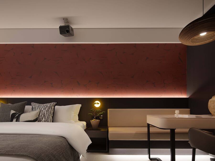 Una habitación de hotel moderna con cama, mesita de noche y un pequeño rincón de descanso.