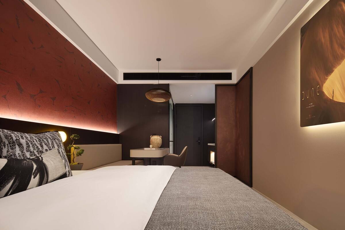 Een moderne hotelkamer met een groot bed, een tafeltje met een vaas, een stoel en een kunstwerk aan de muur.