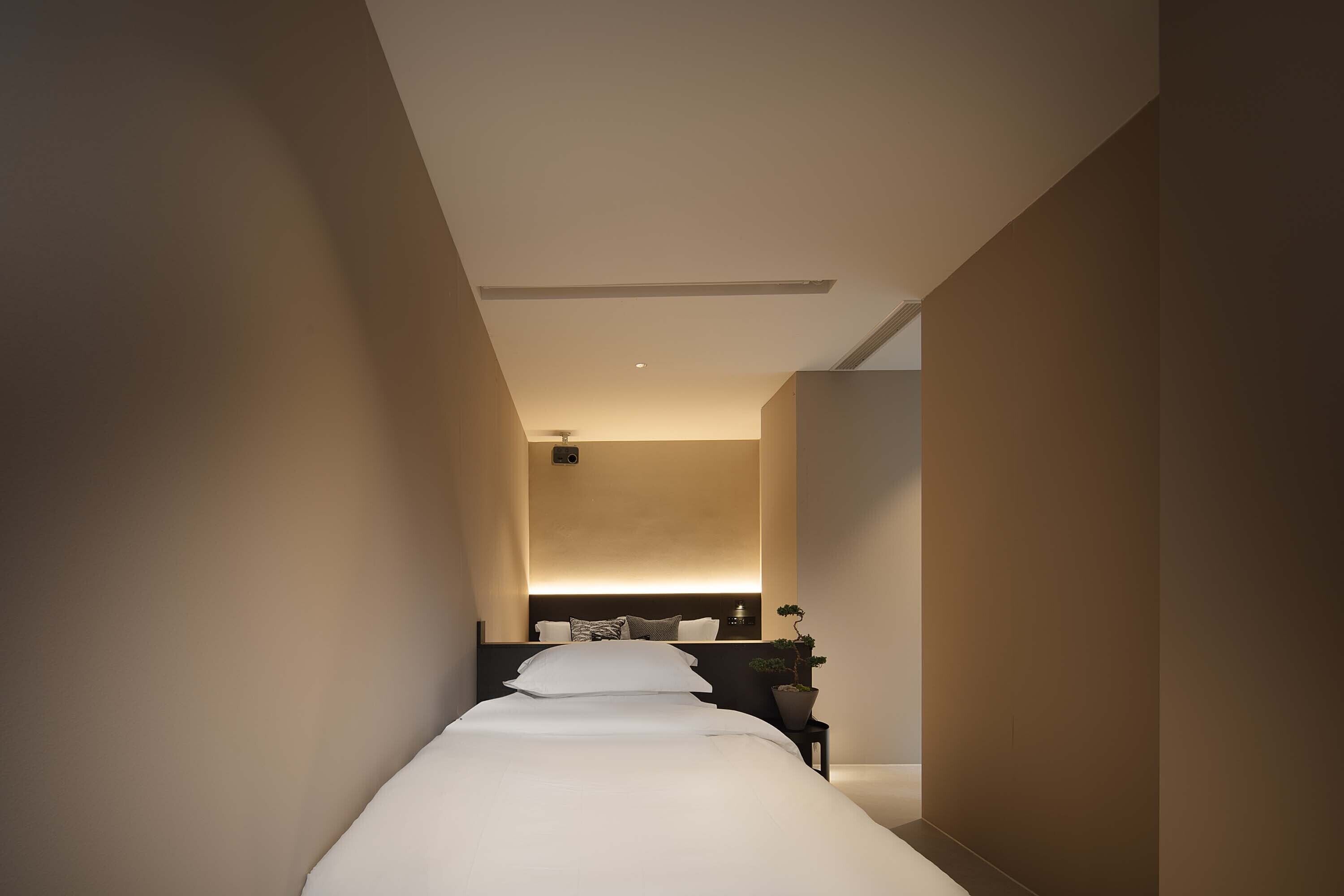 Un pasillo estrecho que conduce a un dormitorio con una cama, una mesita de noche y una planta en maceta.