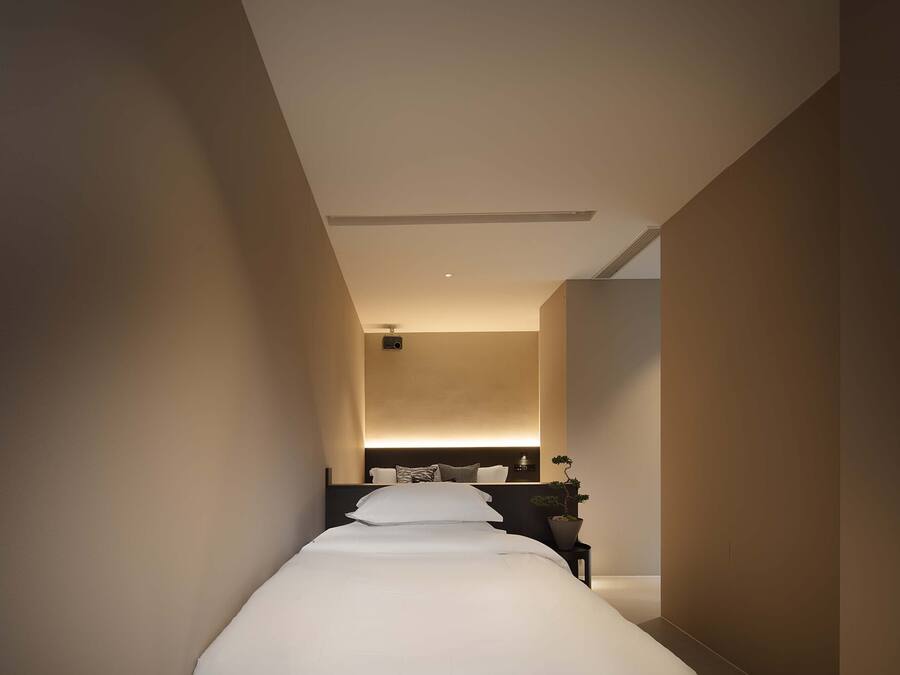 Un pasillo estrecho que conduce a un dormitorio con una cama, una mesita de noche y una planta en maceta.