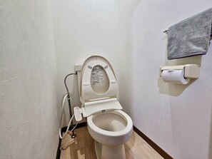 Un baño pequeño con un inodoro, un secador de manos y una toalla colgada en la pared.