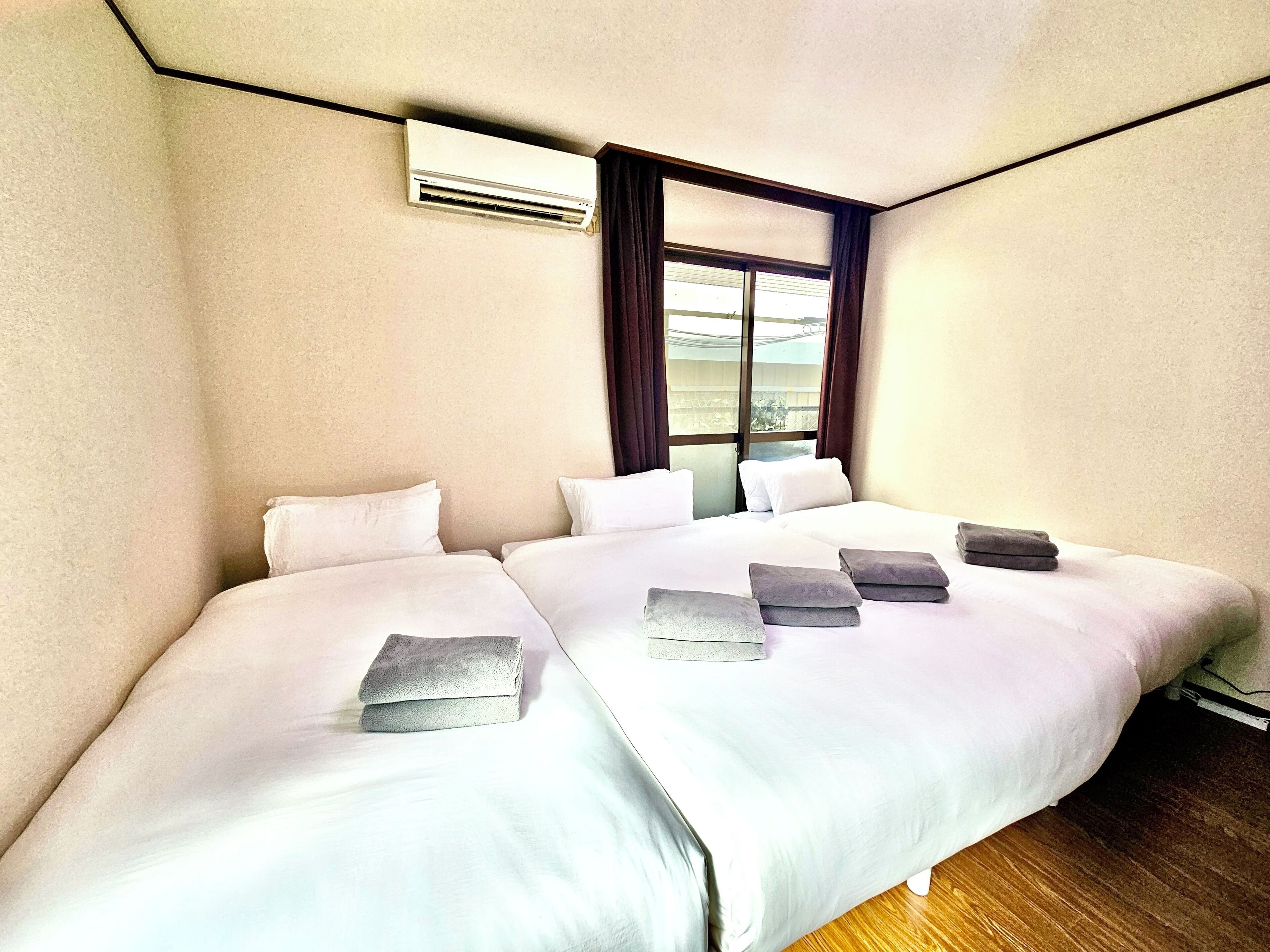 A hotel room with a large bed, a window with curtains, an air conditioning unit, and a wooden floor.