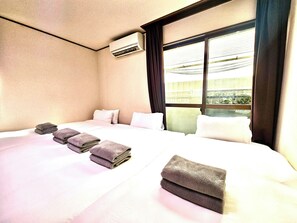 Habitación de hotel con una cama grande, un equipo de aire acondicionado, un ventanal con vistas a un edificio y toallas dobladas con cuidado.