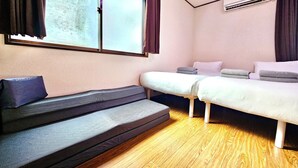 Ein Zimmer mit einem Bett, einem Schlafsofa, einem Fenster mit Vorhängen, einer Klimaanlage und einem Holzboden.