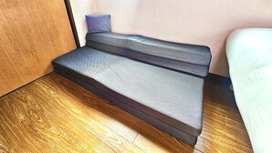 Ein gemütlicher Raum mit Holzboden, einem Bett mit weißer Matratze und einem grauen Sofa mit Kissen.