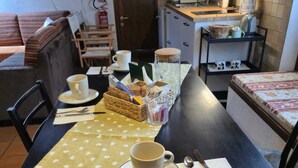 A dining table set with a cup, saucer, spoon, and knife, with a basket of snacks and a glass pitcher. - Cozy attic in quiet area near road junctions and commercial area (Via Pontebbana)