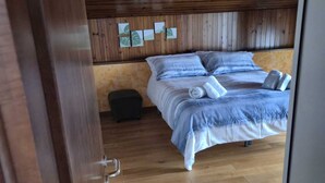 A bedroom with a wooden ceiling, a bed with a blue and white duvet, and a small black trash bin. - Cozy attic in quiet area near road junctions and commercial area (Via Pontebbana)