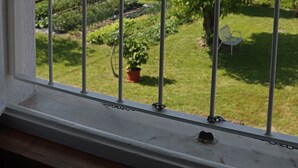 A view through a window with a metal railing, featuring a garden with various plants and a building in the background. - Cozy attic in quiet area near road junctions and commercial area (Via Pontebbana)