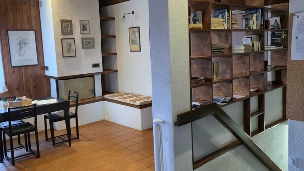 A room with a wooden ceiling, a dining area with a table and chairs, and a bookshelf filled with books and decorative items. - Cozy attic in quiet area near road junctions and commercial area (Via Pontebbana)