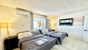 Camera d'albergo con due letti, una TV, una lampada e una finestra con persiane.