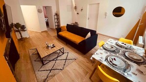 A living room with a sofa, a dining table set for four, and a staircase leading to another room. - Le Ch`ti Cambrai, Logement Élégant, Centre ville (Cambrai)