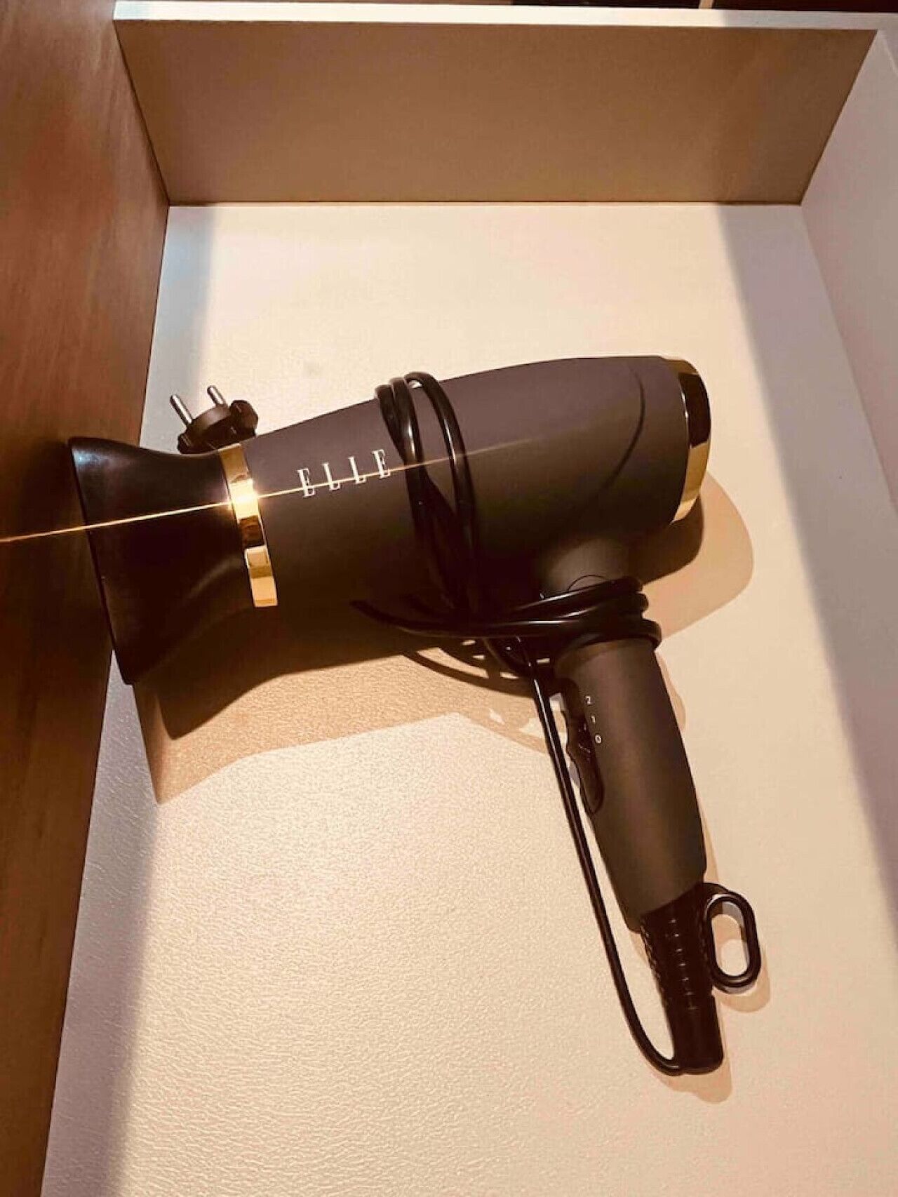 Un sèche-cheveux noir avec des détails dorés, présenté dans une boîte blanche.