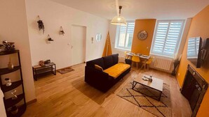 A spacious living room with a black sofa, wooden flooring, a dining area with a yellow chair, and a fireplace. - Le Ch`ti Cambrai, Logement Élégant, Centre ville (Cambrai)
