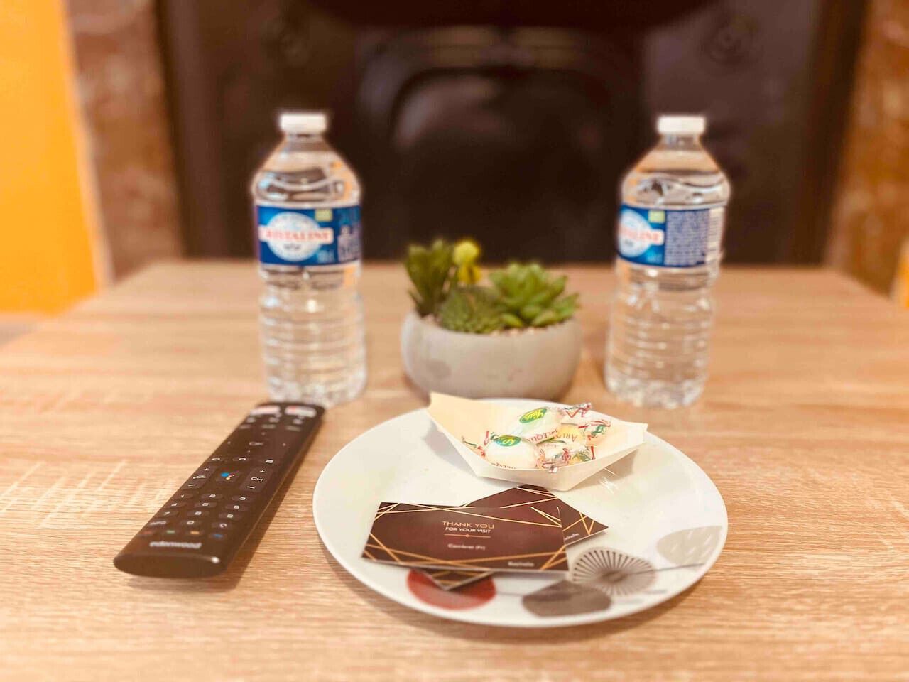 Ein Tisch mit einer Fernbedienung, einer Snackplatte, einer Dankeskarte und zwei Wasserflaschen.