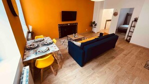 A modern living room with a sofa, dining table, and chairs. There is a fireplace and a television mounted on the wall. - Le Ch`ti Cambrai, Logement Élégant, Centre ville (Cambrai)