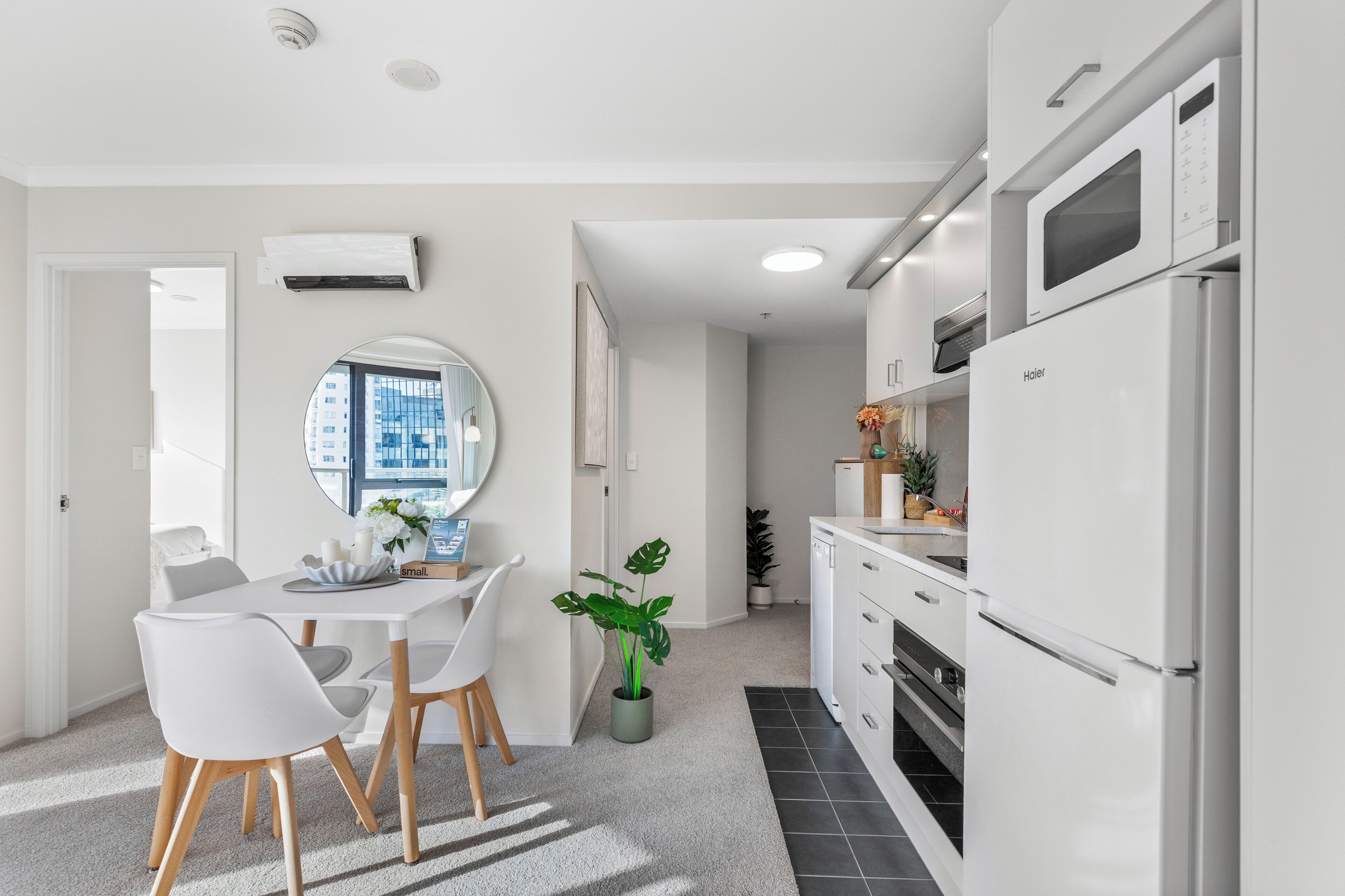 A modern kitchen with white appliances, a dining area with a white table and chairs, and a potted plant.