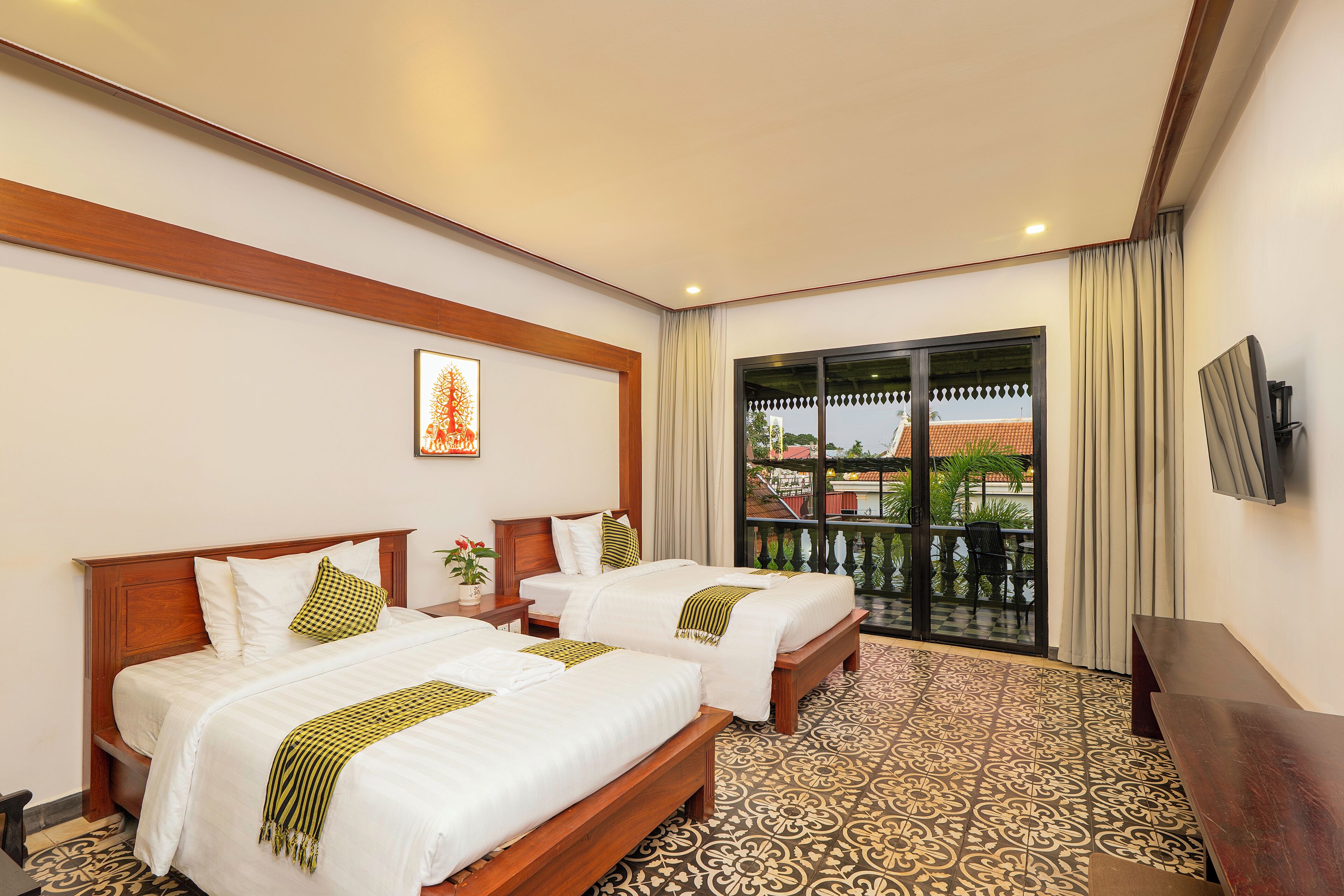 A hotel room with two beds, a TV, a balcony with a view, and patterned flooring.