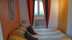 Un dormitorio con cama, ropa de cama colorida, una ventana con cortinas, aire acondicionado instalado en la pared y una lámpara.