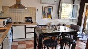 Una cocina compacta con microondas, tostadora y cafetera sobre la encimera. Hay una mesa de comedor con sillas y una pequeña ventana con cortinas.