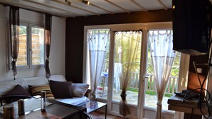 Una habitación con sofá, mesa y televisor. Hay cortinas en las ventanas.
