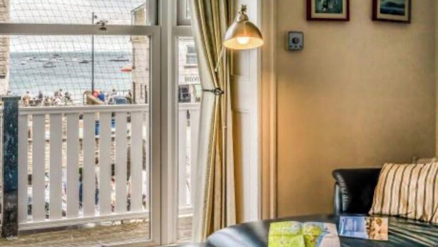 Ein Hotelzimmer mit großem Fenster und Blick auf einen Strand, einem Bett, einer Lampe und einigen gerahmten Bildern an der Wand.