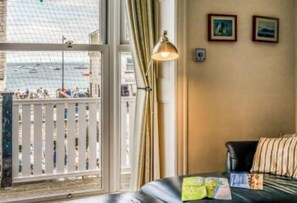 Une chambre d’hôtel avec une grande fenêtre donnant sur une plage, un lit, une lampe et quelques tableaux encadrés accrochés au mur.