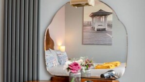 Ein Zimmer mit einem runden Spiegel, der ein Bett, einen Nachttisch und eine Wandlampe reflektiert.