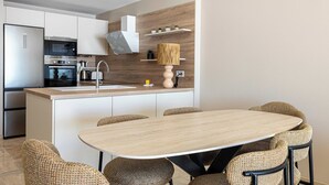 Et moderne køkken med ø, indbyggede hårde hvidevarer og spiseplads med fletstole.